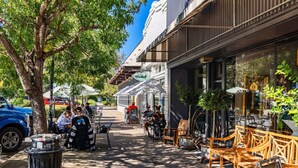 Ein Straßencafé mit Tischen, Stühlen und einem Papierkorb. In der Nähe ist ein Auto geparkt.
