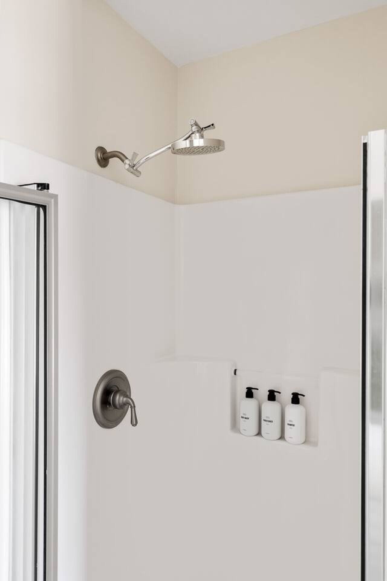 Un ducha moderna con cabezal de ducha de mano y grifería empotrada. Hay tres botellas de champú y acondicionador en la pared.