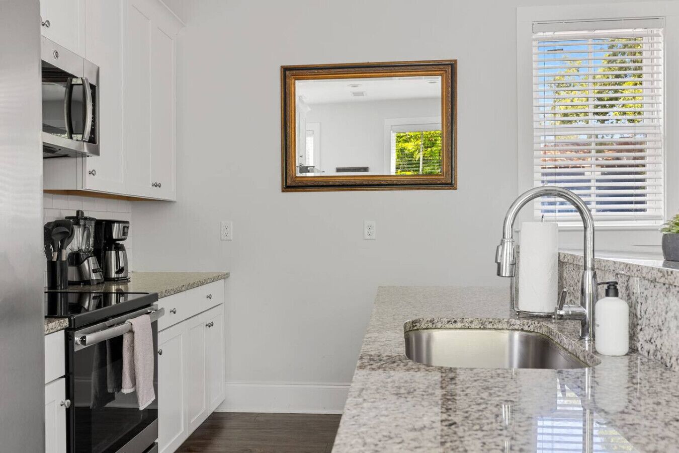 A kitchen with white cabinets, a stainless steel sink, a coffee maker, and a microwave.