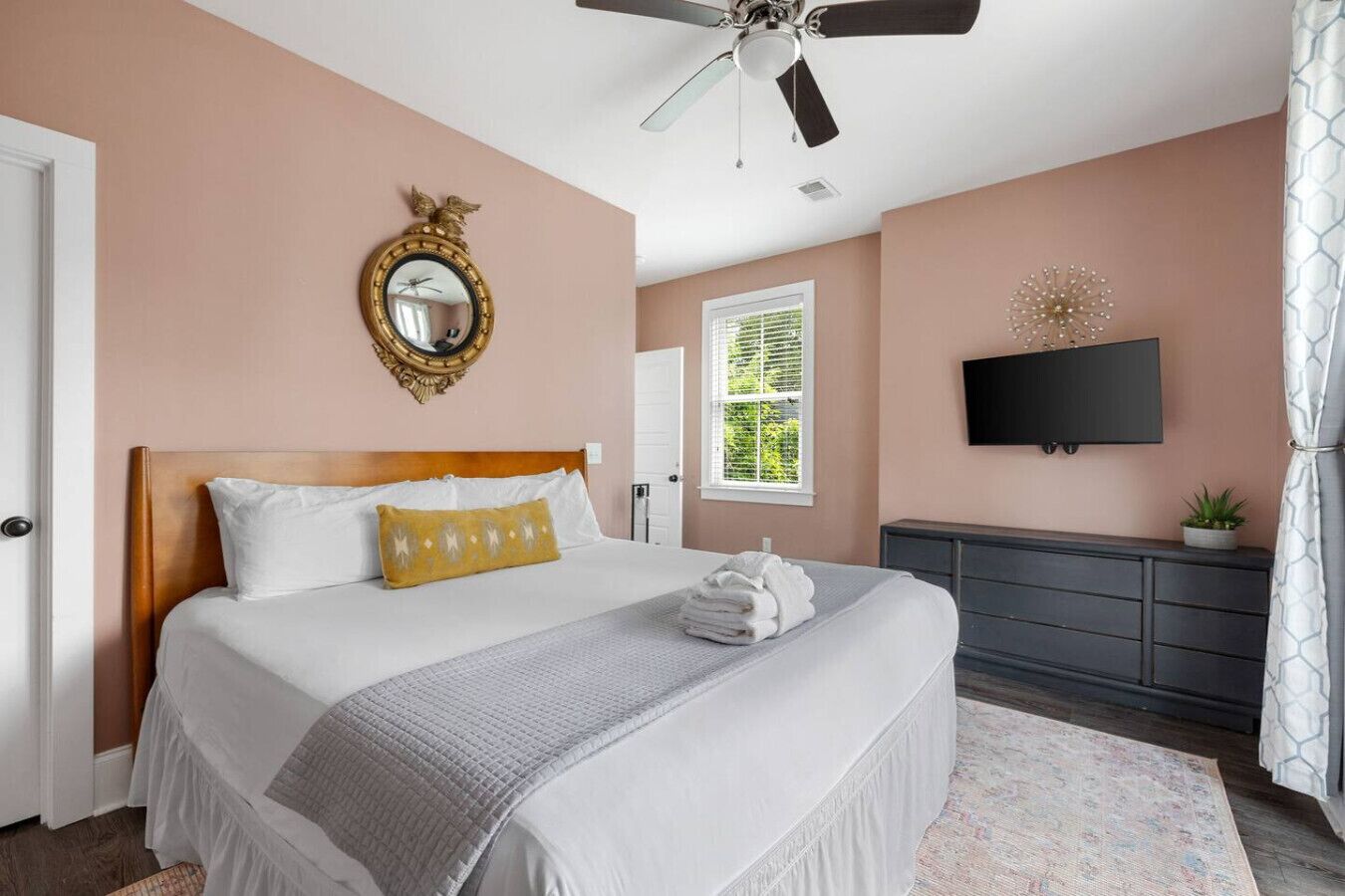 A bedroom with a bed, a ceiling fan, a TV, a dresser, and a window with blinds.