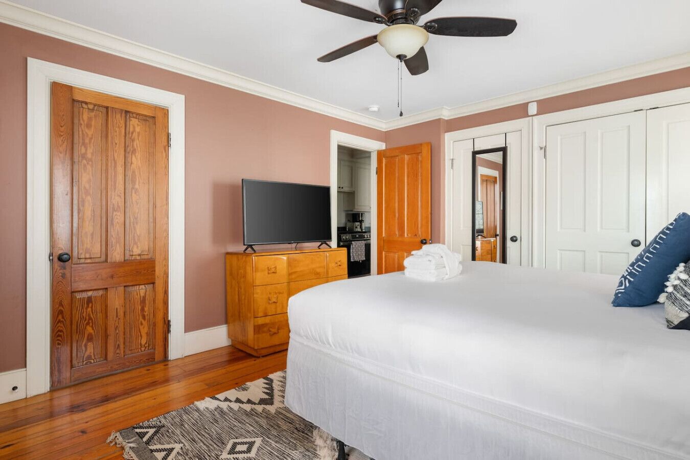 A bedroom with a bed, a dresser, a television, and a ceiling fan.