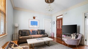 A living room with a sofa, coffee table, and armchairs, a television, and a chandelier. - 2BR/2BA Downtown Charleston on Spring St + Parking (Charleston)