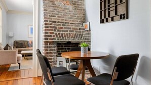 A dining area with a brick wall, a round table, and two black chairs. - 2BR/2BA Downtown Charleston on Spring St + Parking (Charleston)