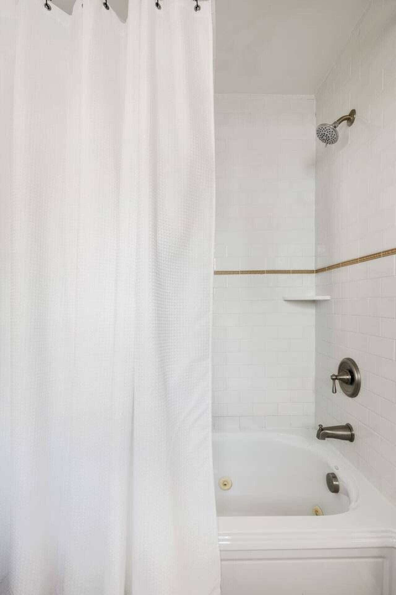Un baño con una bañera blanca, un cabezal de ducha y una cortina.
