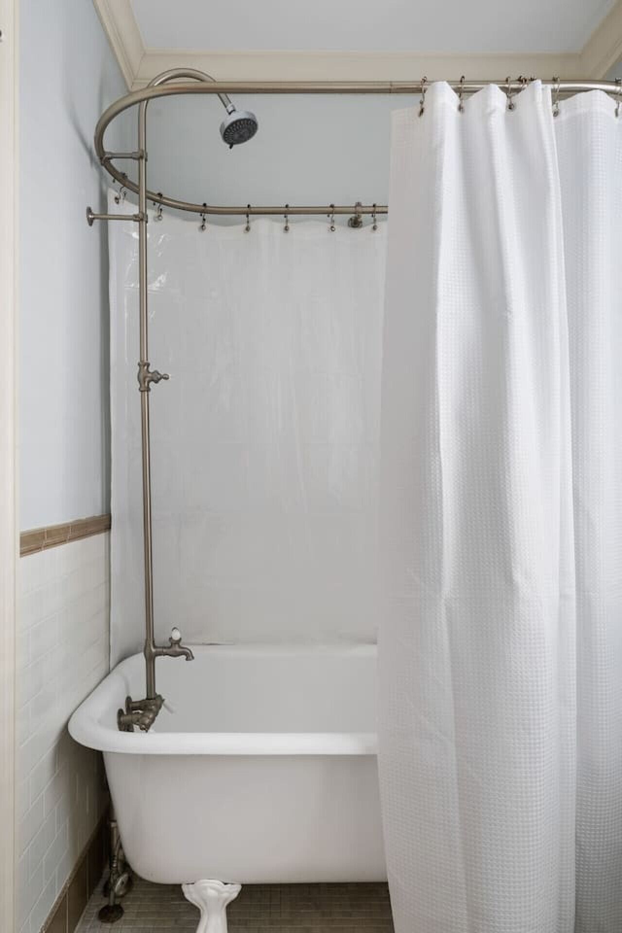 Een kleine, afgesloten badkamer met een witte badkuip, douchekop en douchegordijn.