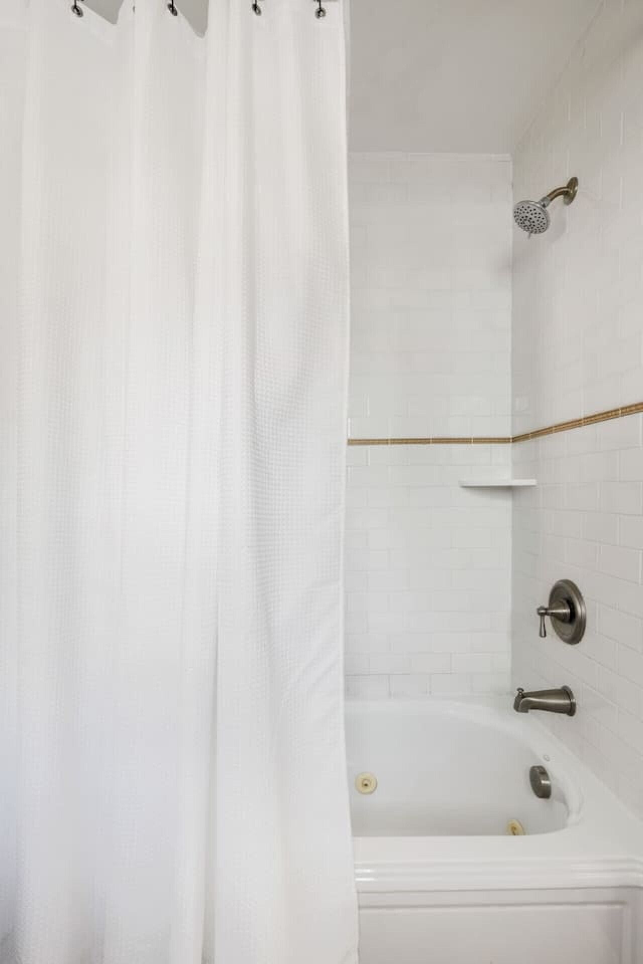 A bathroom with a white bathtub, a showerhead, and a curtain.