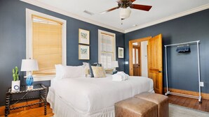 Quarto com cama grande, mesas de cabeceira, ventoinha no teto e porta de madeira.