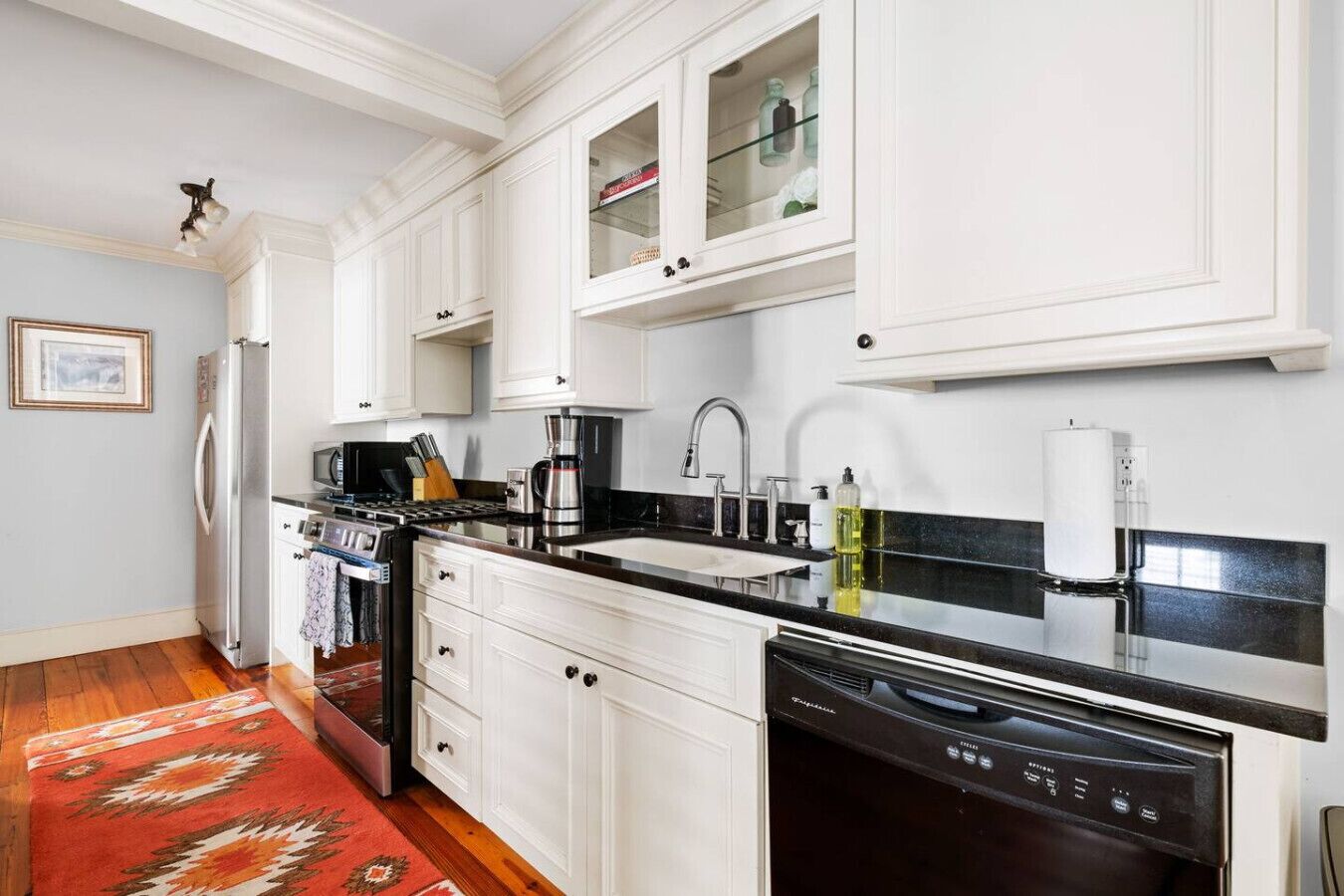 A modern kitchen with white cabinetry, a black countertop, and a red rug.