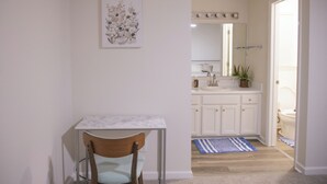 A small, clean room with a single chair, a table, a white cabinet, a mirror, and a door leading to a bathroom.
