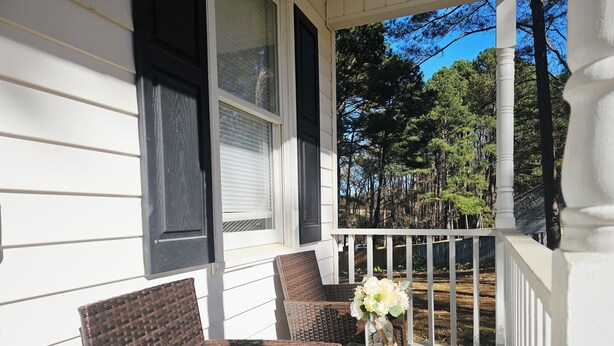 A porch with wicker furniture and a glass table, overlooking a wooded area.