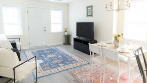 A living room with a TV, dining table, chairs, a ceiling fan, and a large window.