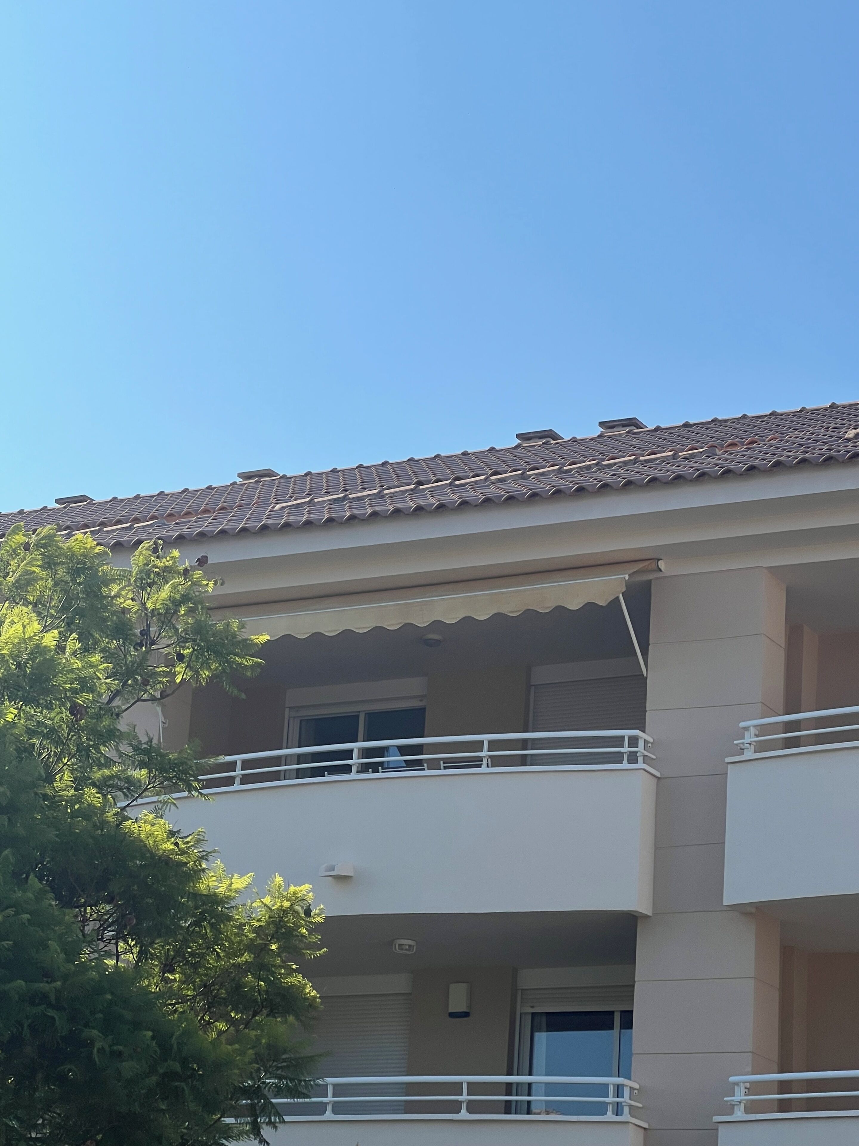 A multi-story building with a tiled roof, balconies with railings, and a clear sky.