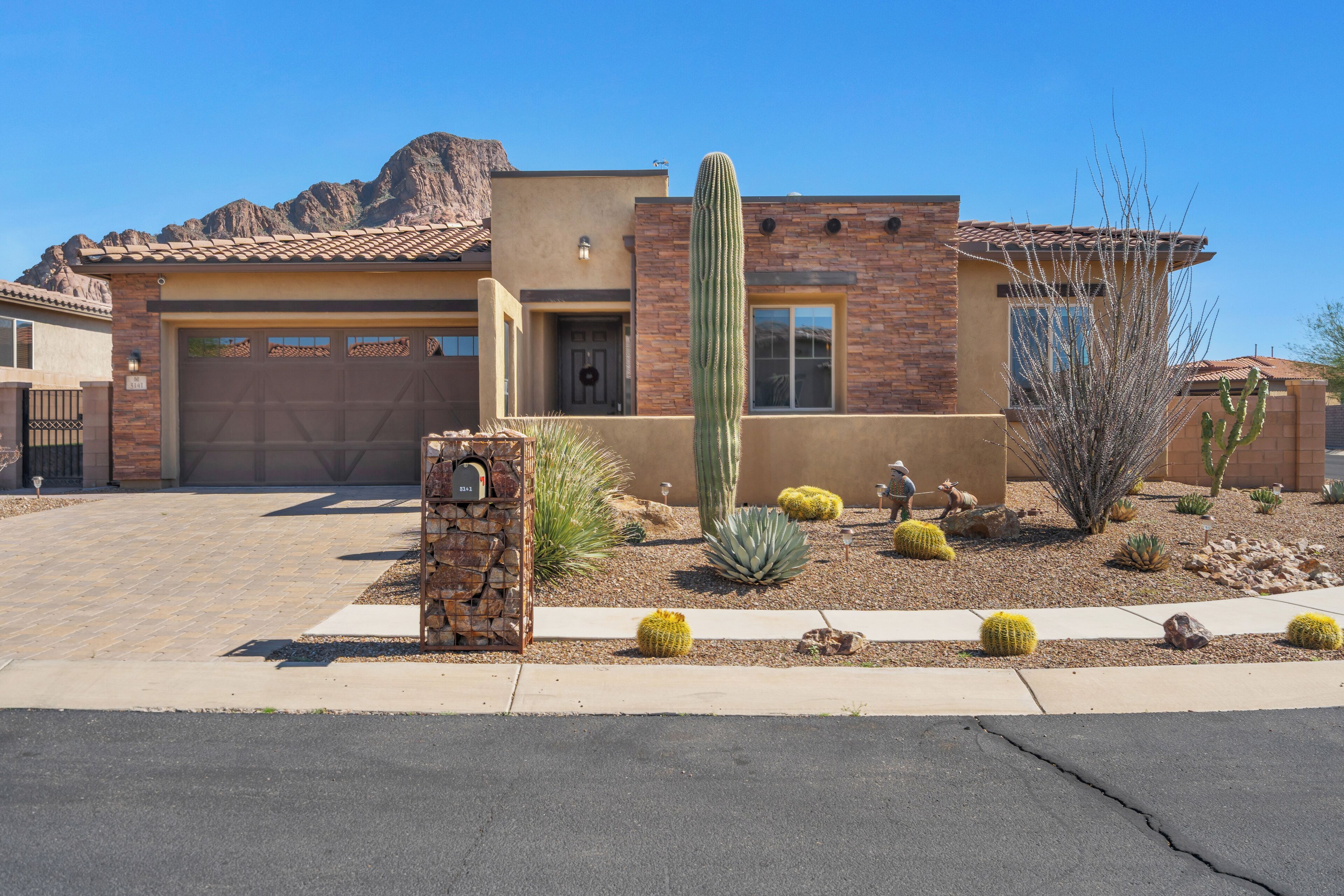 A two-story house with a garage, a large cactus garden, and a mountain backdrop.