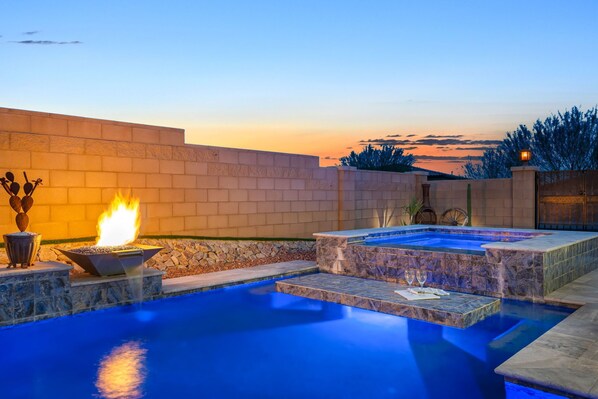 A swimming pool with a fire feature and a hot tub, surrounded by stone walls and a sunset view. - Starr Ridge Snowbird Home! Heated Pool & Spa! 30+Nights! (Tucson)