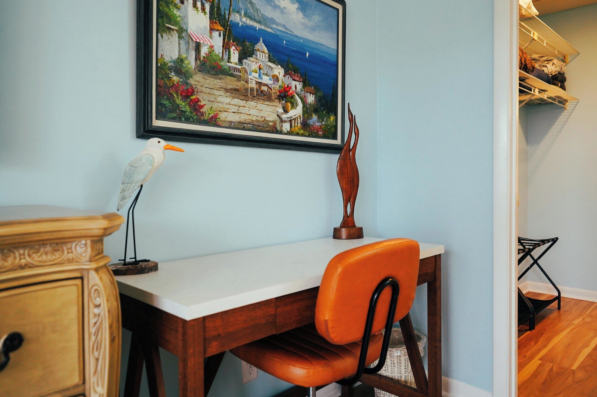 A room with a desk, chair, and a framed painting on the wall.