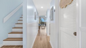 A hallway with a staircase, a door with a sign, and a view to a balcony. - Sandy Sea Turtle Pet-Friendly Condo w/ Ocean Views (St. Augustine Beach)