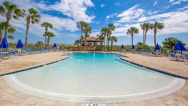 A swimming pool with lounge chairs and umbrellas, surrounded by palm trees. - Sandy Sea Turtle Pet-Friendly Condo w/ Ocean Views (St. Augustine Beach)