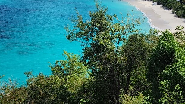 Paesaggio costiero con acque turchesi, una spiaggia sabbiosa e colline verdi e rigogliose.