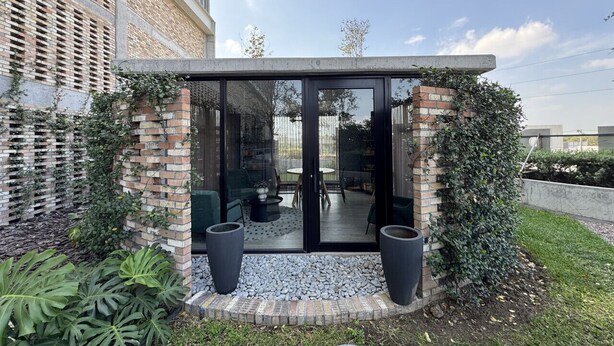 A modern outdoor seating area with a glass enclosure, surrounded by a brick wall and greenery. - Dpto. cerca de Ternium y UANL (Monterrey)