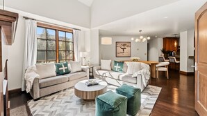 A spacious living room with a large window, a dining area, and a kitchen. - Beaver Creek Penthouse | Pool, Hot Tub, Walkable (Avon)
