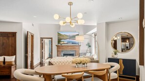 A dining area with a wooden table and chairs, a fireplace, and a large painting on the wall. - Beaver Creek Penthouse | Pool, Hot Tub, Walkable (Avon)