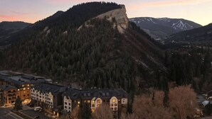 A hotel with multiple floors, a parking lot, and a mountain backdrop. - Beaver Creek Penthouse | Pool, Hot Tub, Walkable (Avon)