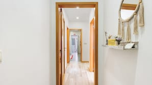 A hallway with wooden doors, a wooden floor, a wall-mounted macrame decoration, and a small shelf with a plant and a sign. - Tour House – Rio Tinto: Cozy Retreat for a Relaxing Stay (Rio Tinto)