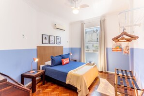 Une chambre à coucher avec un lit, une tête de lit en bois, une table de chevet avec une lampe, un fauteuil suspendu et une fenêtre avec des rideaux.