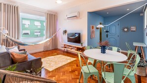 A modern living room with a hammock, a flat-screen TV, a round dining table with chairs, and a blue accent wall. - 2bdrs With Copacabana Beach View A 2936/1202 (Rio de Janeiro)