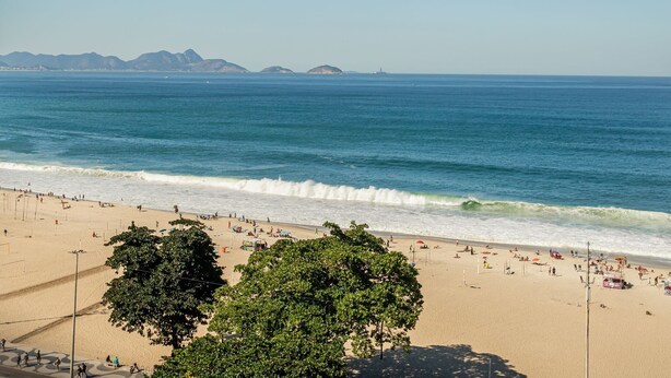 A beach with clear blue water, sandy shore, and distant mountains. - 2bdrs With Copacabana Beach View A 2936/1202 (Rio de Janeiro)