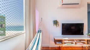 A room with a large window overlooking a beach, a hammock, a flat-screen TV, and a small shelf with books. - 2bdrs With Copacabana Beach View A 2936/1202 (Rio de Janeiro)