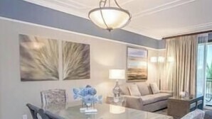 A dining area with a glass table, chairs, and a chandelier. There is a sofa and a lamp in the background. - Rare Luxurious 3 Bedroom, 3 Bathroom Condo on Marco Island, FL (Marco Island)