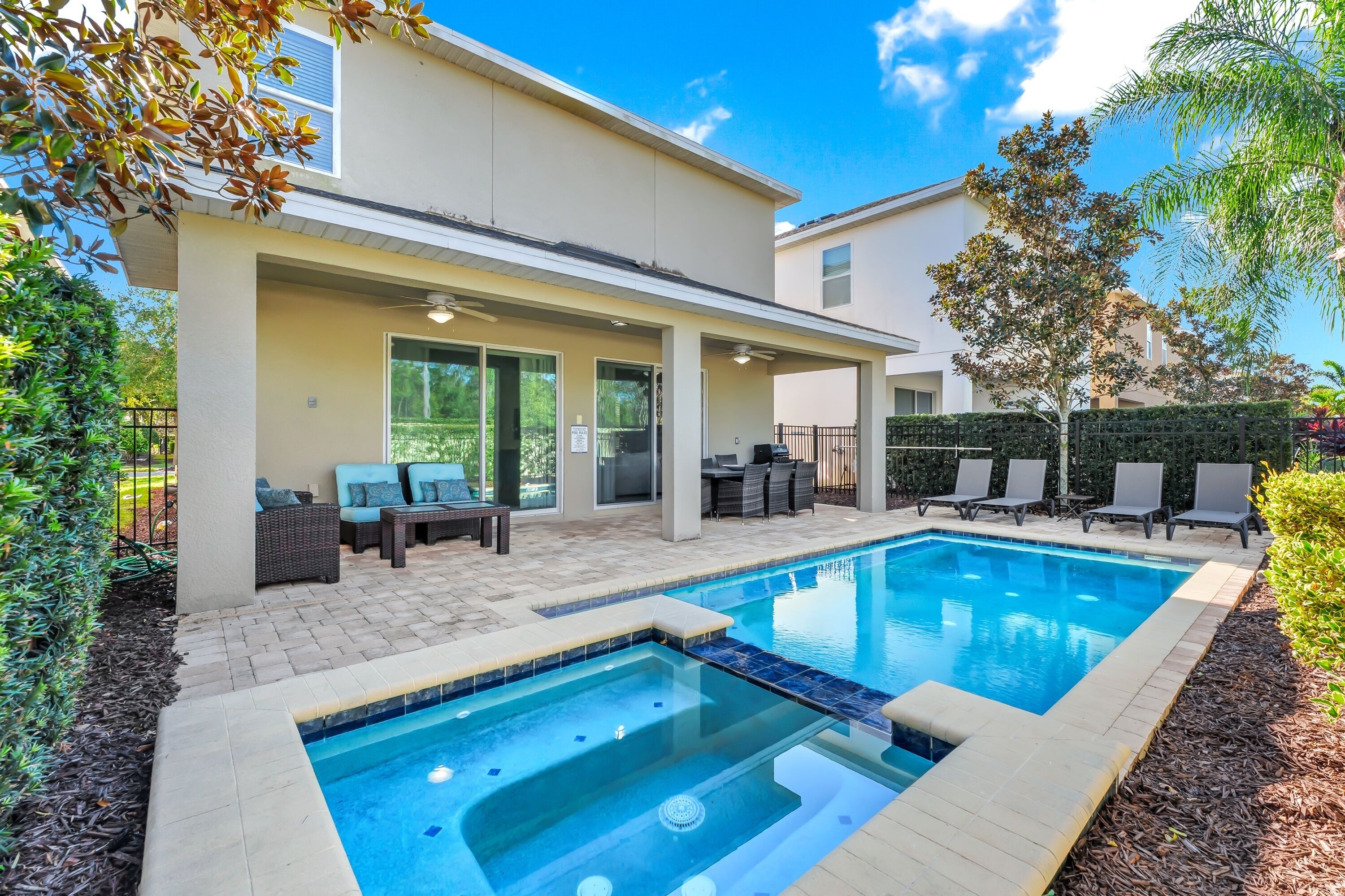 A modern outdoor pool area with a hot tub, lounge chairs, and a covered patio.