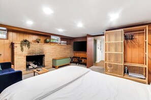 A bedroom with a brick fireplace, a bed, a blue chair, a wooden wardrobe, and a TV on the wall. - Bright 1BR Near UW & Local Parks (Seattle)