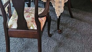 Un coin repas avec une table dressée pour quatre personnes, agrémenté d’une nappe en dentelle, de sets de table rouges et d’une plante en pot.