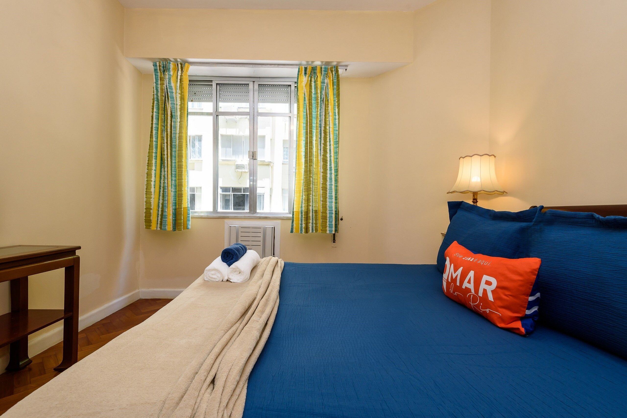 Une chambre à coucher avec un lit, une table de chevet, une lampe et une fenêtre avec des rideaux.