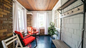 A cozy room with a brick wall, wooden ceiling, and a large window. There are two red chairs, a small table, and a potted plant. - Charming Modern Farmhouse Retreat (Terre Haute)