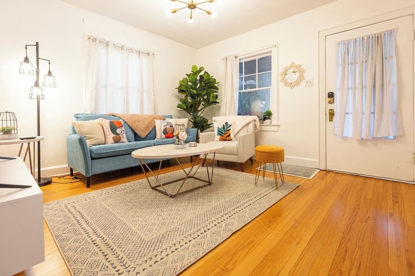 Een woonkamer met een blauwe bank, een witte fauteuil, een bijzettafeltje en een grote plant.