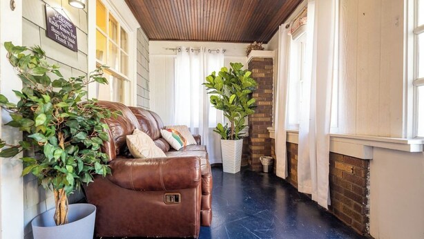 A hallway with a brown leather sofa, potted plants, and a brick fireplace. - Charming Modern Farmhouse Retreat (Terre Haute)