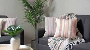 En moderne stue med en grå sofa, stribede puder, et rundt sofabord og en stor plante.