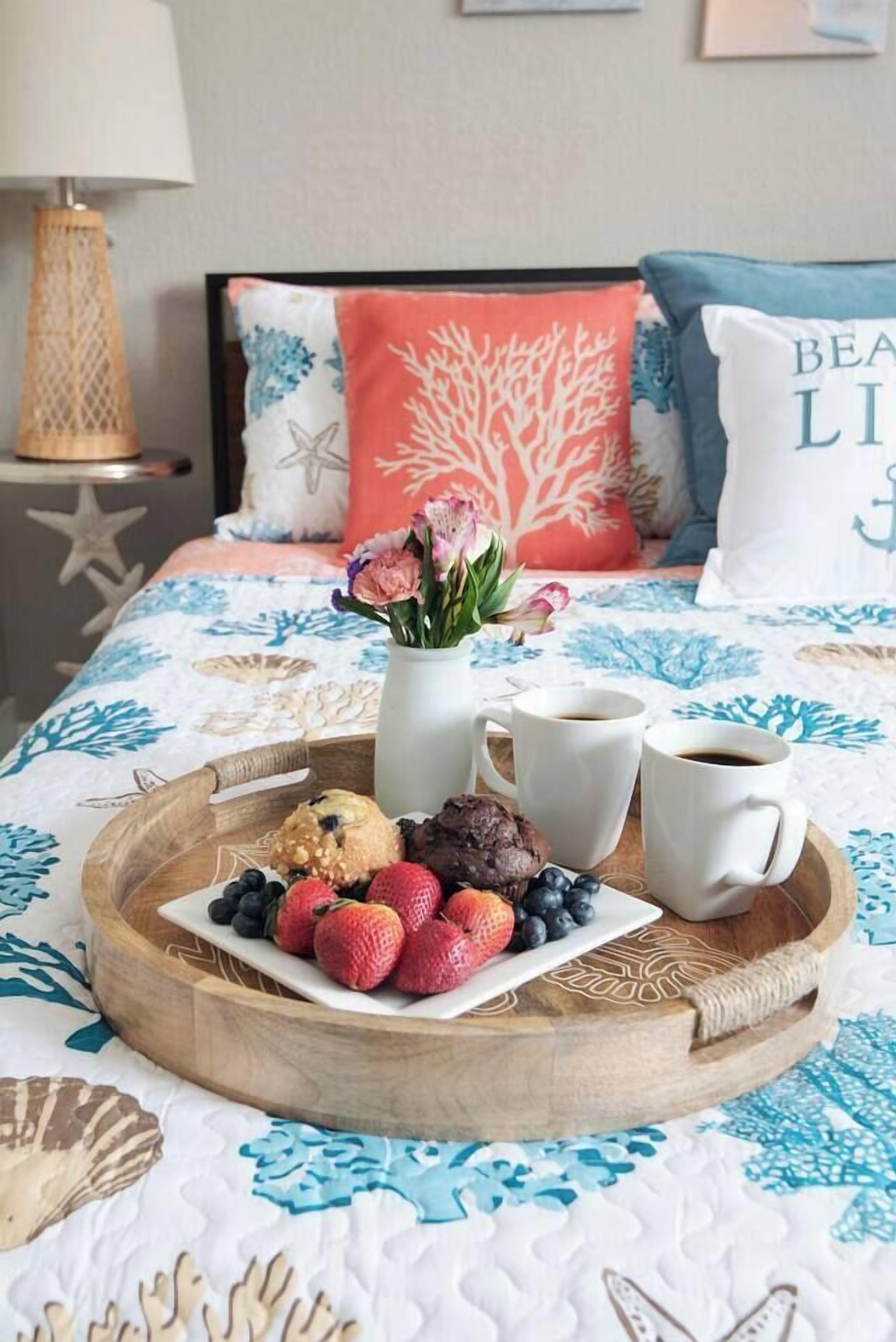 Een bed met een bloemenbedekking, een dienblad met aardbeien, bosbessen en koekjes, en twee koffiemokken.