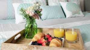En pænt anrettet morgenmadsbakke med croissanter, bær og juice på et sengebord under et kystbillede.
