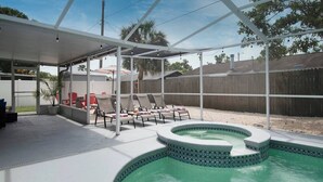 Et overdækket udendørsområde med jacuzzi, liggestole og swimmingpool.