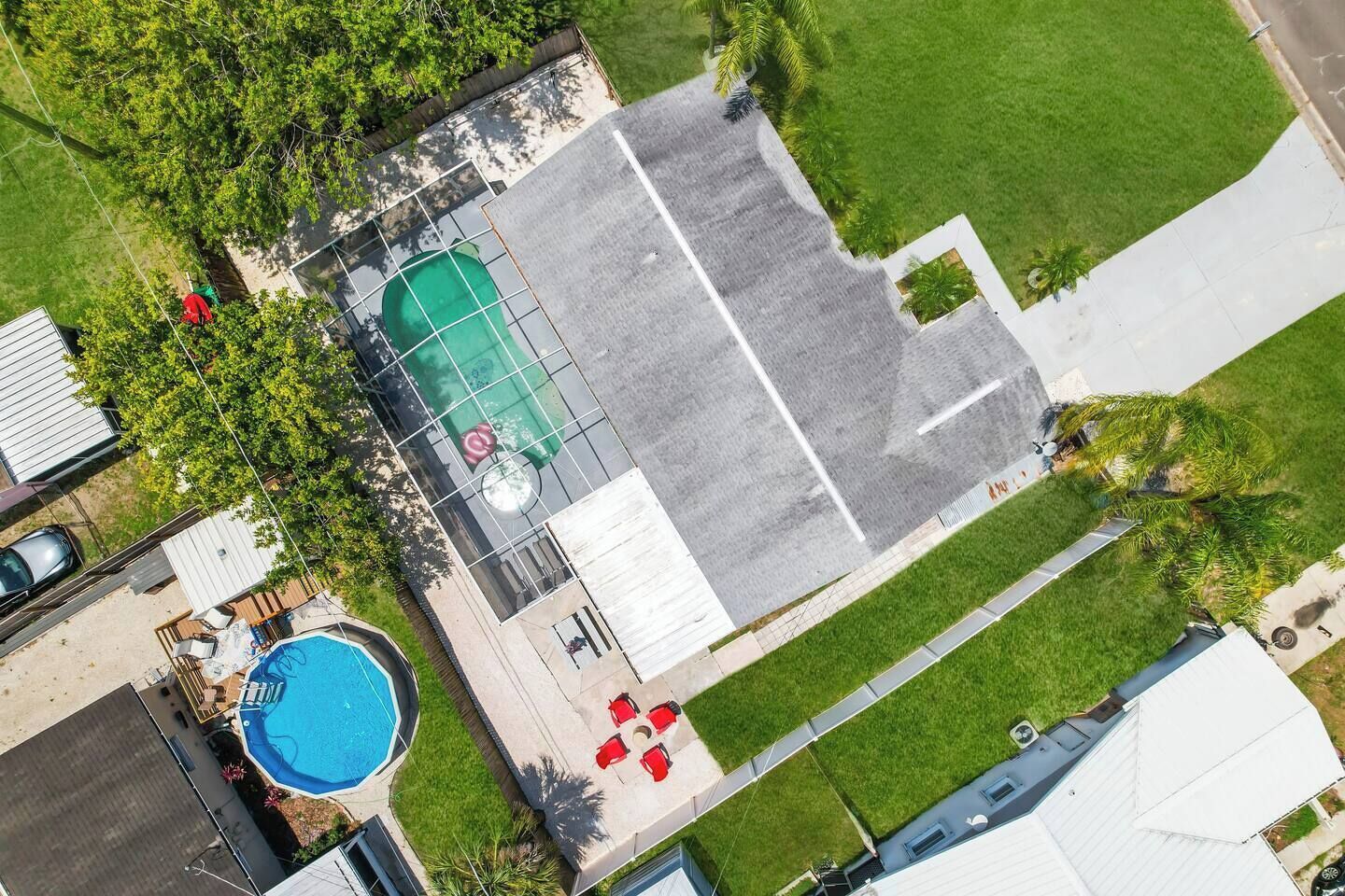 An aerial view of a residential property with a swimming pool, a tennis court, and a covered patio area.