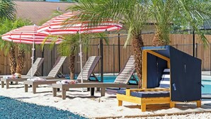 Un espace aménagé au bord de la piscine, avec des chaises longues, des parasols à rayures et un coin salon abrité.