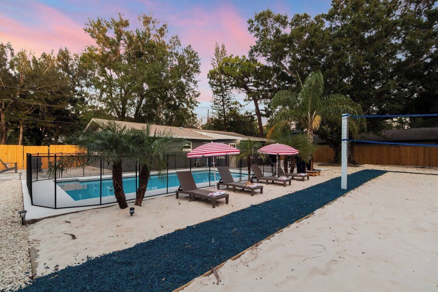 A backyard with a swimming pool, lounge chairs, and umbrellas.