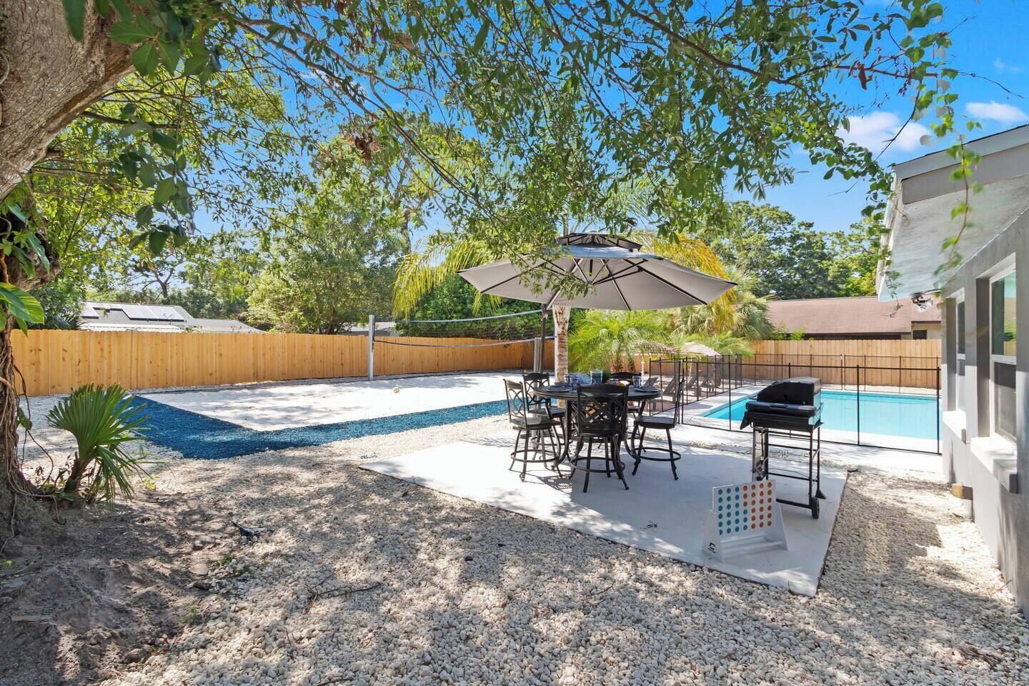 Un patio trasero con piscina, una parrilla y un comedor con mobiliario exterior.