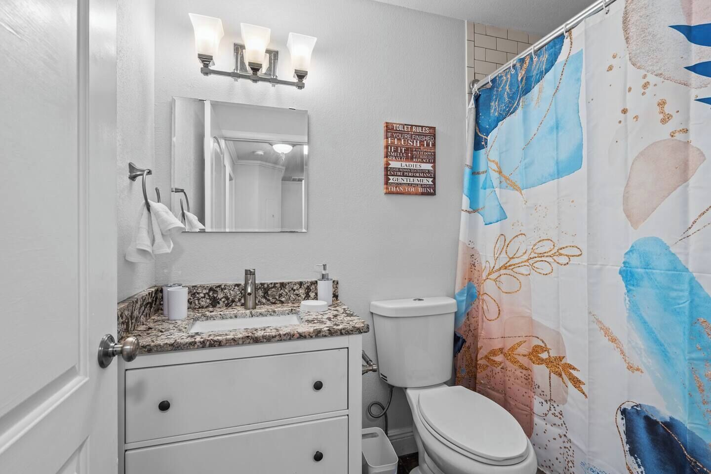 A bathroom with a white vanity, a toilet, and a shower curtain with a floral pattern.