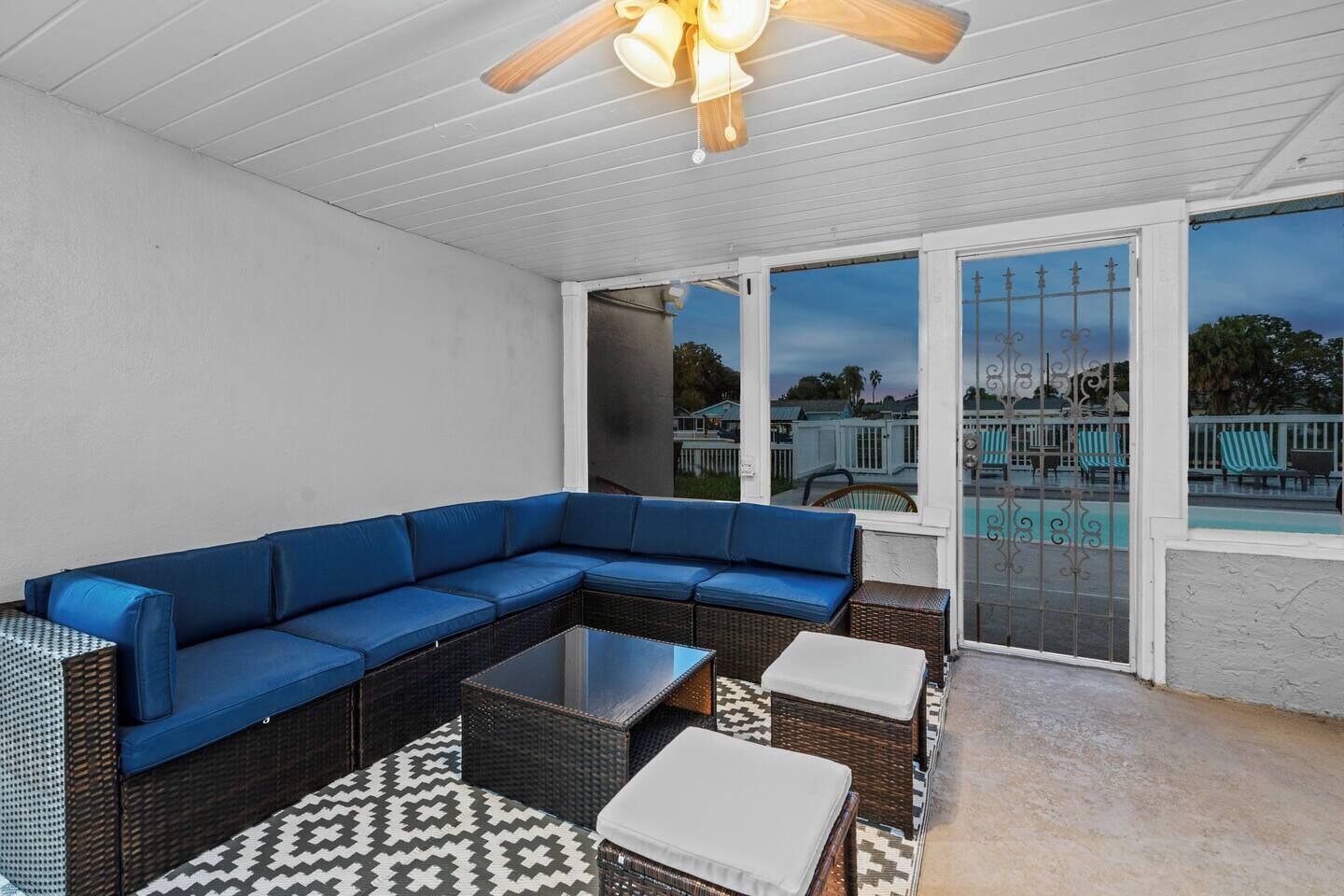 A covered patio with a blue sectional sofa, wicker furniture, and a patterned rug.