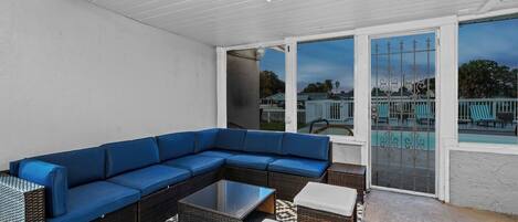 A covered patio with a blue sectional sofa, wicker furniture, and a patterned rug.